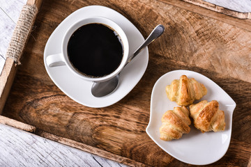 Cup of coffee on wooden tray with croissants.