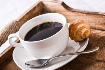 Cup of coffee on wooden tray with croissants.