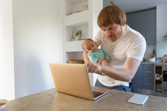 Cheerful New Dad Holding Baby Daughter And Pointing At Laptop Monitor. Family Portrait Of Red Haired Man And Cute Little Child In Home Interior. Media Content Concept