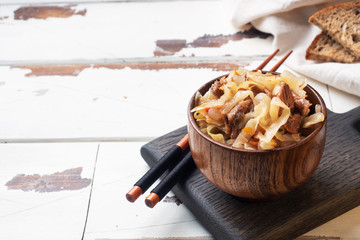 Stewed cabbage with meat in a wooden bowl on a wooden background. Traditional Russian dish of...