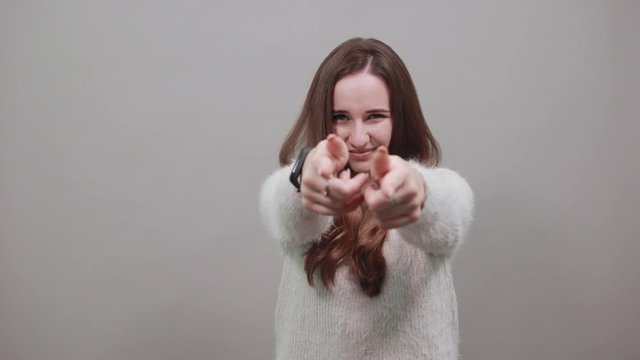 Cheerful caucasian lady wearing sweater isolated on gray background in studio pointing fingers at camera. People emotions, lifestyle concept.