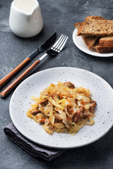 Stewed cabbage with meat on a plate. Dark concrete background.
