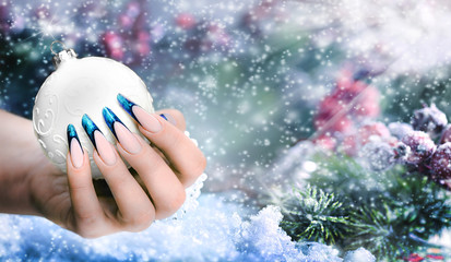 Christmas ball in woman perfect nails used shiny colour snow background, Snowy winter celebration...