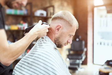 Side view of a man in a stripe cape visiting a barber shop, getting a trendy hairstyle