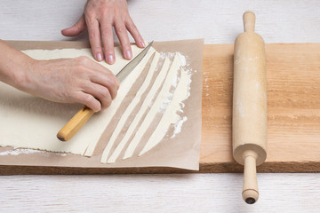 Hand cuts rolled dough into strips with knife. Process of making homemade pasta. .