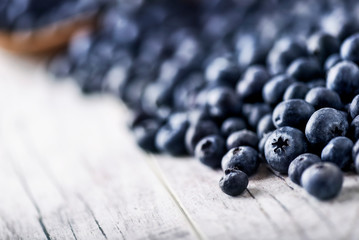 Freshly picked blueberries in wooden bowl on white table. Juicy and fresh blueberry with green leaves at rustic board. Bilberry antioxidant healthy forest food.