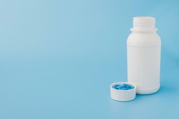 Blue capsules, pills on a blue background. Capsules in a white jar. Vitamins, nutritional supplements for women's health