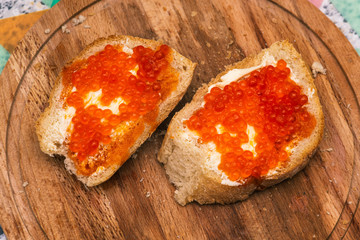 Red caviar on the bread. Bread with butter. Sandwiches with red caviar on a wooden board. Delicious snacks for the holiday
