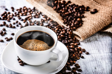 Coffee cup and beans on old white table. Roasted coffee beans top view.