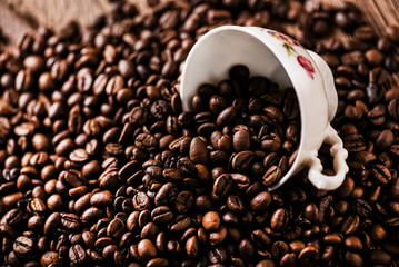 Fresh coffee beans with white cup on wooden background.