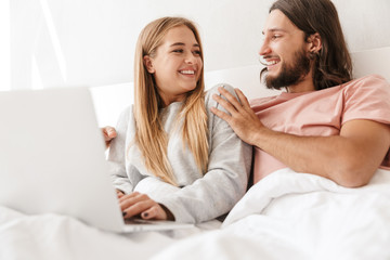 Loving couple in bed using laptop computer indoors at home.