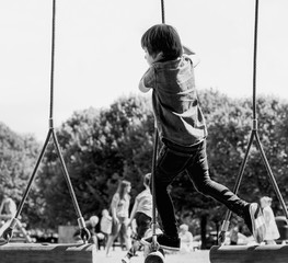 Black and white candid shot of Active kid climbing rope in the playground, High key light of Rare view of Child enjoying activity in a climbing adventure park on summer sunny day.