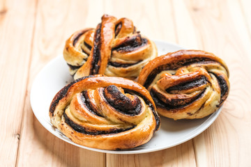 Homemade buns with dark chocolate in a creamic plate with honey on a light wooden background.