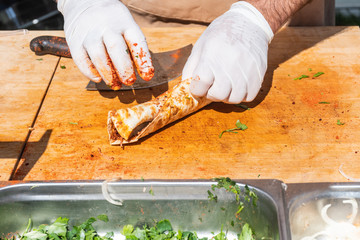 Traditional Turkish pizza, called Lahmacun, being prepared with meat, onion and parsley, displayed on a wooden table at a a street food market