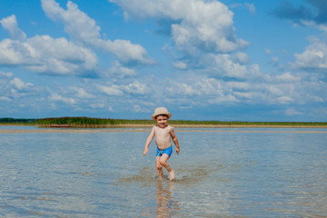 Fototapeta premium Cute little boy running through the water at the beach