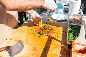Traditional Turkish pizza, called Lahmacun, being prepared with meat, onion and parsley, displayed on a wooden table at a a street food market