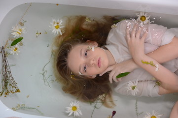 a girl in a white dress is lying in a bath with milk and flowers