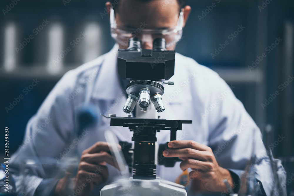 Wall mural young scientist looking through a microscope in a laboratory. young scientist doing some research.