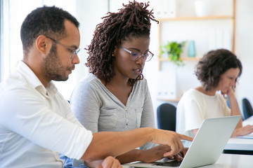 Thoughtful African American employees working with laptop. Side view of focused young woman typing...
