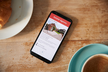 Close Up Of Mobile Phone With Realtors Property App Lying On CafÃ© Table