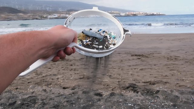 Young man cleaning microplastics from sand on the beach - Environmental problem, pollution and ecolosystem warning concept 