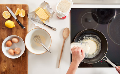 Overhead Shot Of Woman In Kitchen Pouring Batter Into Pan For Pancakes Or Crepes For Pancake Day - Powered by Adobe