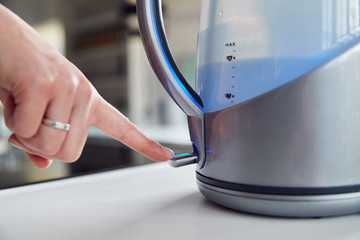 Fototapeta na wymiar Close Up Of Woman Pressing Power Switch On Electric Kettle To Save Energy At Home