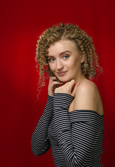 Young cheerful girl with blond curly hair on a bright red background.