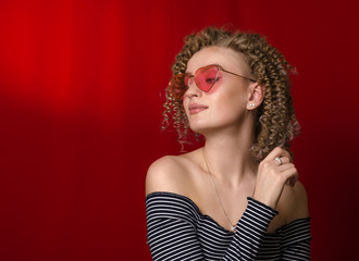 Young girl with blond curly hair in pink glasses on a bright red background,