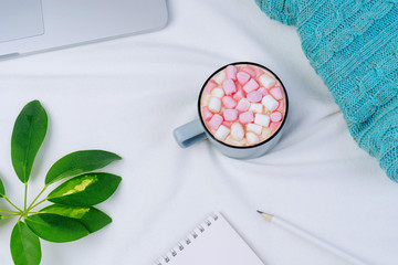 Office workspace with cup of coffee, laptop, knit a blanket and green leaf on white background. Flat lay, top view