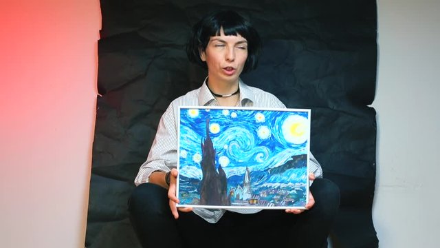 A girl blogger is holding a picture drawn by herself on a black background.