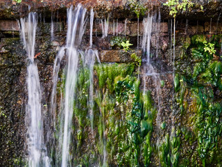 Clear waterfall on old brick wall with green bloom texture background