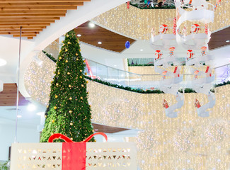 giant christmas tree with gold decoration and big gift box with red  ribbon in shopping mall