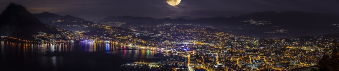 Panoramica della citt&agrave; di Lugano di notte illuminata da una luna brillante