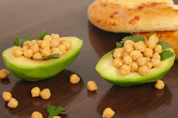 Half cut avocado with boiled chickpeas and parsley inside, vegan diet meal on wooden background....