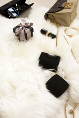 Women's fashion accessories flat lay top view on fur,  wooden background: gift box, handbag, sunglasses, bracelet and cosmetics. copy space