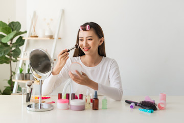 Young female blogger with makeup cosmetics recording video at home