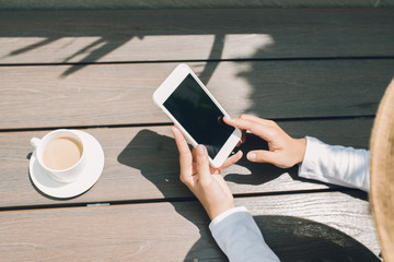 Mockup image of hands holding black mobile under the sun at coffee shop