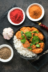 Chicken tikka masala traditional Asian spicy meat food with rice tomatoes and cilantro in a black bowl on dark background. Top view.