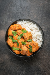Chicken tikka masala traditional Asian spicy meat food with rice tomatoes and cilantro in a black bowl on dark background. Top view.