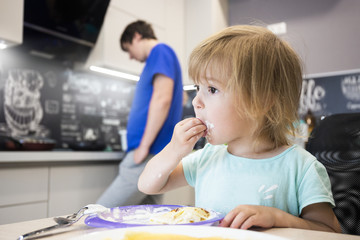 Child eats pancakes cooked by dad in the kitchen with pleasure