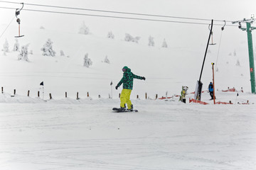 Snowboarder man with colorful outfit riding on piste on a snowy cold day on the first day of the new year. T-bar lift on the background. Kartalkaya, Turkey.