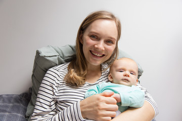 Front of happy joyful new mother holding sweet baby. Portrait of young woman and cute little child in home interior. Baby care concept