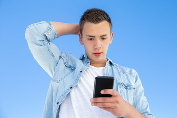 Shocked student guy using smartphone, staring at screen. Handsome young man in casual standing...