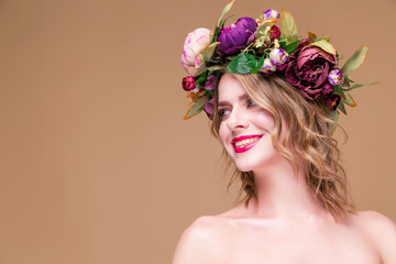 Happy beautiful young woman model with bright flowers on her head smile on the ocher color...