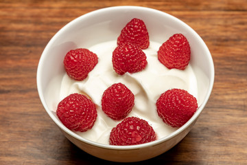 Cottage cheese with raspberries in a white bowl on a wooden table.