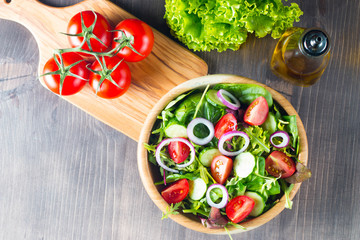 Fresh healthy salad with delicious ruccola, spinach, cabbage, arugula, feta cheese, red onion, cucumber, sesame seeds and cherry tomato on wooden background. Healthy and diet food concept.