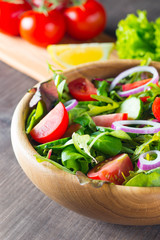 Fresh healthy salad with delicious ruccola, spinach, cabbage, arugula, feta cheese, red onion, cucumber, sesame seeds and cherry tomato on wooden background. Healthy and diet food concept.