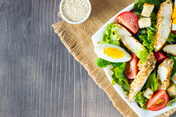 Fresh Caesar salad with delicious chicken breast, ruccola, spinach, cabbage, arugula, egg, parmesan and cherry tomato on wooden background. Oil, salt and pepper. Healthy and diet food concept.