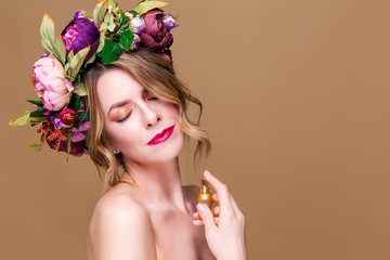 close-up portrait of young woman in floral wreath spraying perfume isolated on ocher background